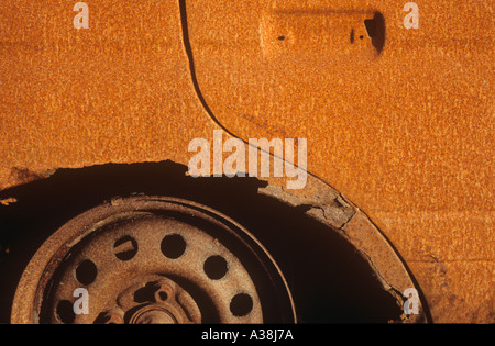 Detail of a rusted burnt out vehicle in the sun showing part of a door panel and wheel arch with hub Stock Photo