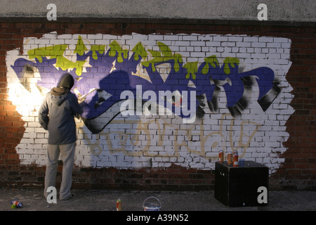 Graffitti Tag artist at work with spray paint can wearing hooded top and protective face mask Belfast Northern Ireland Stock Photo