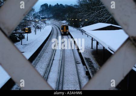 A diesel train pulling into a snow covered Hythe station in Kent England. Station is seen through the wooden cross of the bridge Stock Photo