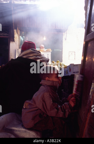 A young boy reads a paper while his father sells fruit in the souk, Fes, Morocco. Stock Photo