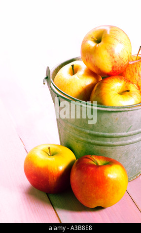 RED YELLOW APPLES IN RUSTIC BUCKET ON COLOUR WASH WOODEN BACKGROUND Stock Photo