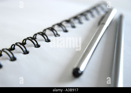 White note book with black spiral binding, stainless steel pen and silver pencil. Shot with shallow depth-of-field. Stock Photo