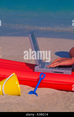 Hand typing on Notebook computer with floating mattress and beach toys by the beach 2803 015 22 Stock Photo