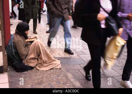 People walk past homeless man begging street in London England UK Stock Photo