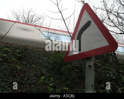 Virgin train on westcountry mainline passing near to bend in road warning sign Stock Photo