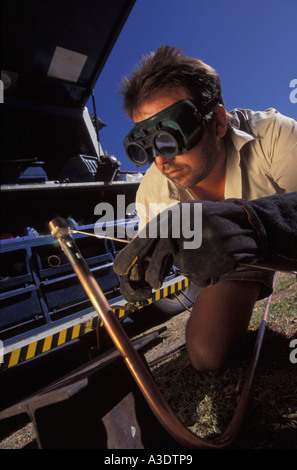 Man brazing a copper pipe outdoors, wearing safety goggles and gloves, Sydney, Australia Stock Photo