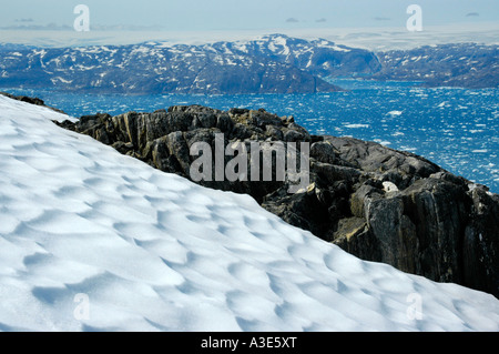 Wide open view over a snow field and rocks to icebergs in Sermilik Fjord Eastgreenland