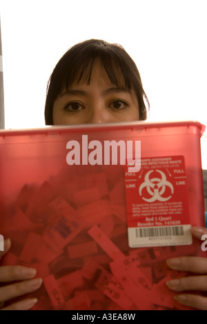 Nurse or healthcare worker holds a Sharps container containing used needles. Stock Photo