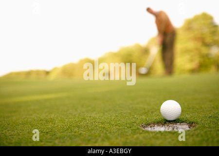 Close-up of a golf ball on the edge of a hole with a man standing in the background Stock Photo