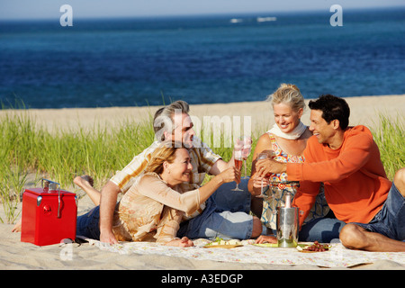 Two mature couples sitting on the beach and toasting with champagne Stock Photo