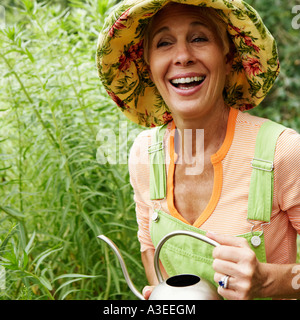 Close-up of a senior woman watering plants and laughing Stock Photo