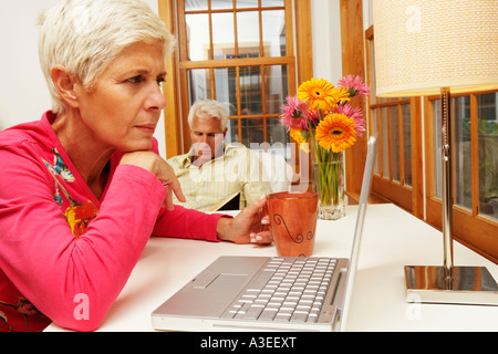 Close-up of a senior woman looking at a laptop with a mature man sitting behind her Stock Photo