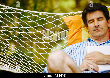 Mature man holding a magazine and sleeping in a hammock Stock Photo