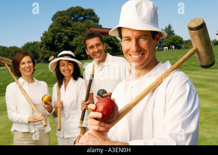 Portrait of a mid adult man holding a croquet mallet and a ball with a mature couple and a mid adult woman standing behind him Stock Photo