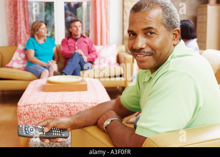 Portrait of a mature man operating a remote control with three mature people sitting beside him Stock Photo
