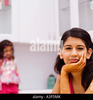 Portrait of a young woman with her hand on her chin with a girl sitting in the background Stock Photo