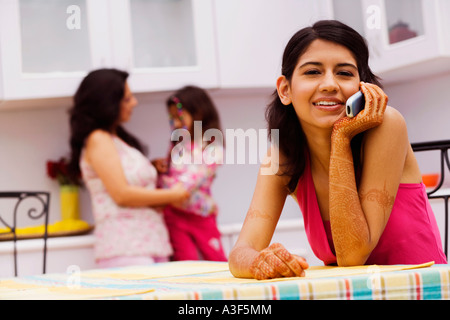 Portrait of a young woman talking on a mobile phone and a mid adult woman standing with her daughter in the background Stock Photo