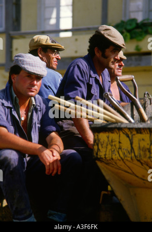 Algarve Portugal blue overalled workmen set off for roadworks wearing traditional flat caps Stock Photo