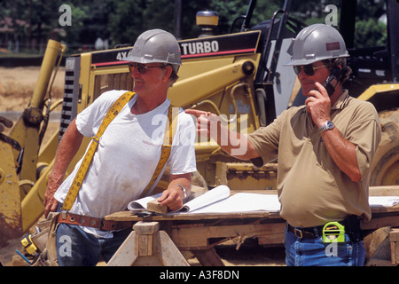Engineer Pointing Out Something to Construction Supervisor While on Mobile Phone at Job Site United States Stock Photo