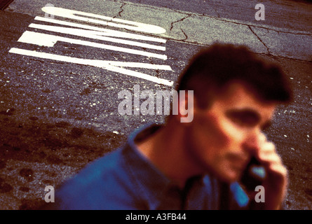 Man alone talks on phone with only written on the street behind him Stock Photo