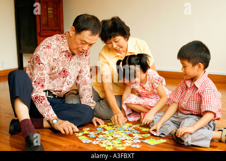 Girl and a boy playing jigsaw puzzle with their grandparents Stock Photo