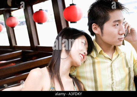 Close-up of a young man talking on mobile phone and a young woman resting her head on his shoulder Stock Photo