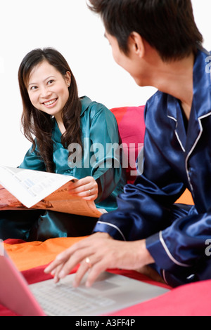 Close-up of a young woman reading newspaper and a mid adult man using a laptop Stock Photo