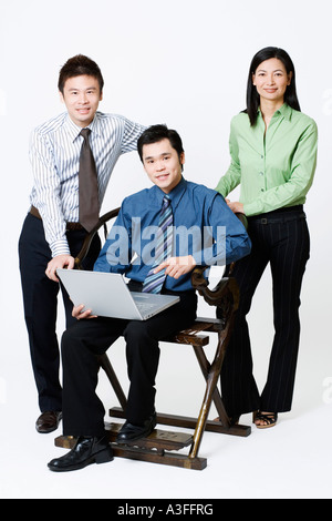 Portrait of a businessman holding a laptop with two businesspeople standing beside him Stock Photo