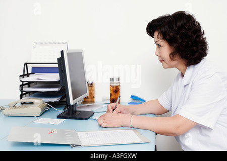 Close-up of a female doctor looking at a computer monitor and writing on a notepad Stock Photo