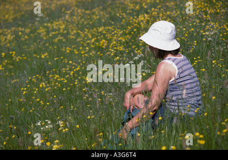 Middle aged female sits among mixed"wild flowers" on a hot day Stock Photo