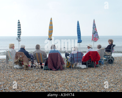 South of England resort group of senior citizens seated on beach perhaps optimistic that sun is going to shine and parasols can be opened England UK Stock Photo