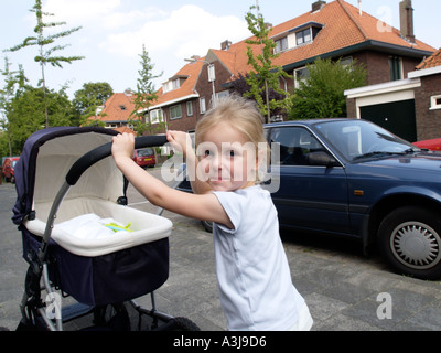 Little girl four years old pushing her little baby sister along in the streets of Breda the Netherlands Stock Photo