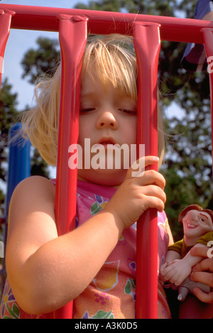 Girl age 2 looking through bars on playground. St Paul Minnesota USA Stock Photo