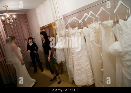 A young woman looks at herself in a mirror as she tries on a white wedding dress in a store in New York USA January 2006 Stock Photo