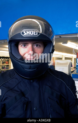 Smiling young man wearing motorcycle helmet and jacket with workplace in background Stock Photo