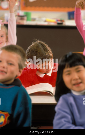 Caucasian Asian American Latino students raising hands in class while one male student is having difficulty Stock Photo