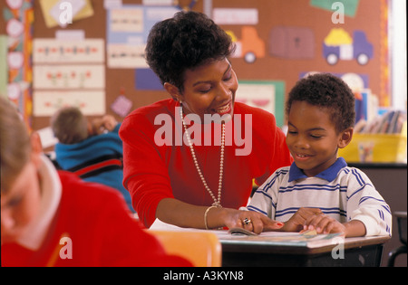 African American teacher assisting male student in elementary classroom Stock Photo