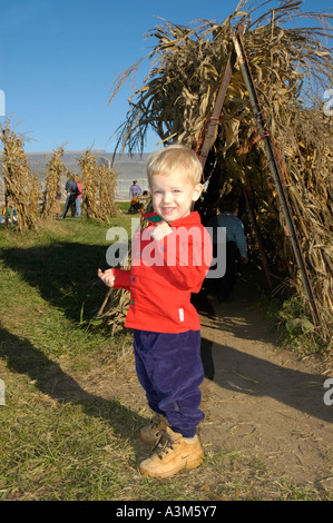 Young blond boy playing near corn tunnel at a fall farm harvest event Stock Photo