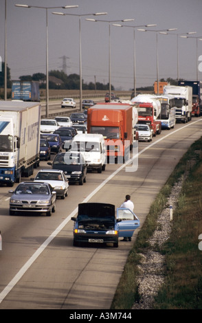 Aerial view long queue of M25 motorway car lorry truck van traffic gridlocked in jam with driver beside broken down car on hard shoulder England UK Stock Photo