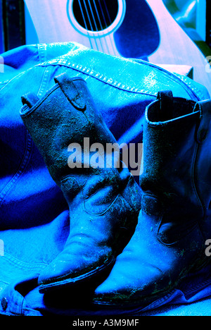 Cowboy boots covered in dried hay and grass and worn out leather in blue light with an old guitar Canada Stock Photo