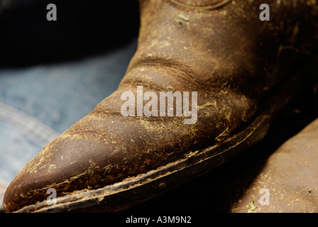 Cowboy boots covered in dried hay and grass and worn out leather Canada Stock Photo