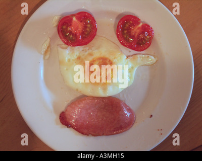 Tomatoes fried egg bacon on white plate forming a face Stock Photo