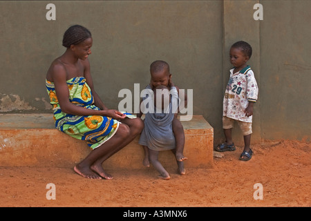 Happy African mother from Ghana and baby toddler hugging slightly older brother with another brother looking on Stock Photo