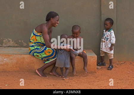 Happy African mother and baby toddler from Ghana with slightly older brother and another brother looking on Stock Photo