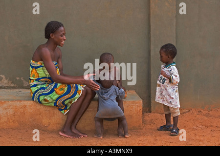 Happy African mother and baby toddler from Ghana hugging slightly older brother with another brother looking on Stock Photo