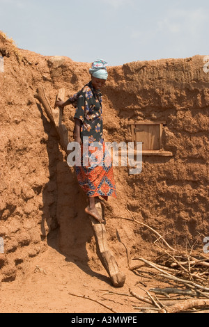 Village woman, Larabanga, Ghana, using ridgid ladder made from tree trunk to get down from her house roof. Stock Photo