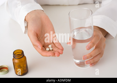 A young woman's hand holding a glass of water and pills Stock Photo