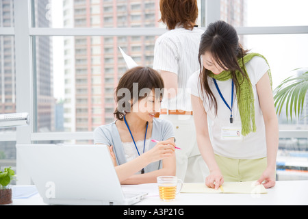 Two young women looking at notebook and young man standing behind Stock Photo