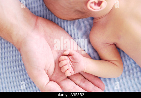 Closeup of newborn baby sleeping on blue blanket with adults hand under tiny arm Stock Photo
