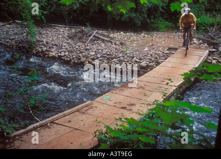 A mountain biker crosses a bridge over a river near Marquette Michigan Stock Photo